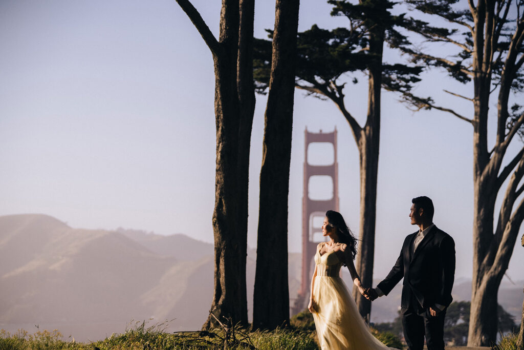 Couple walking along the tree lines with Golden Gate Bridge in the background.