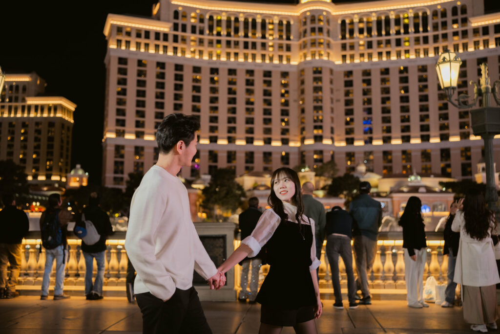 Couple holding hands at night in front of the lit Bellagio hotel during their Bellagio fountain engagement photos session