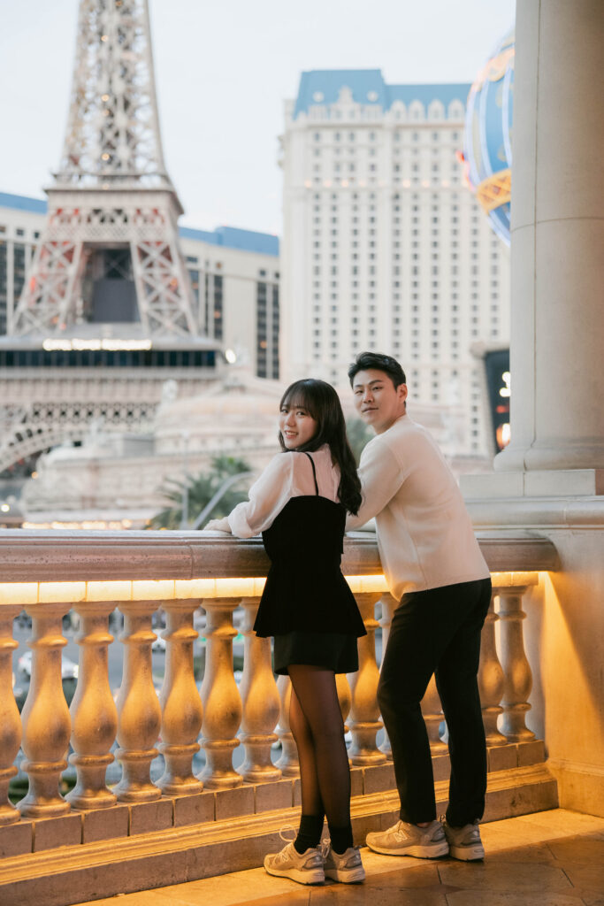 Engaged couple leaning on a stone balustrade at blue hour with the Paris Las Vegas Eiffel Tower behind them