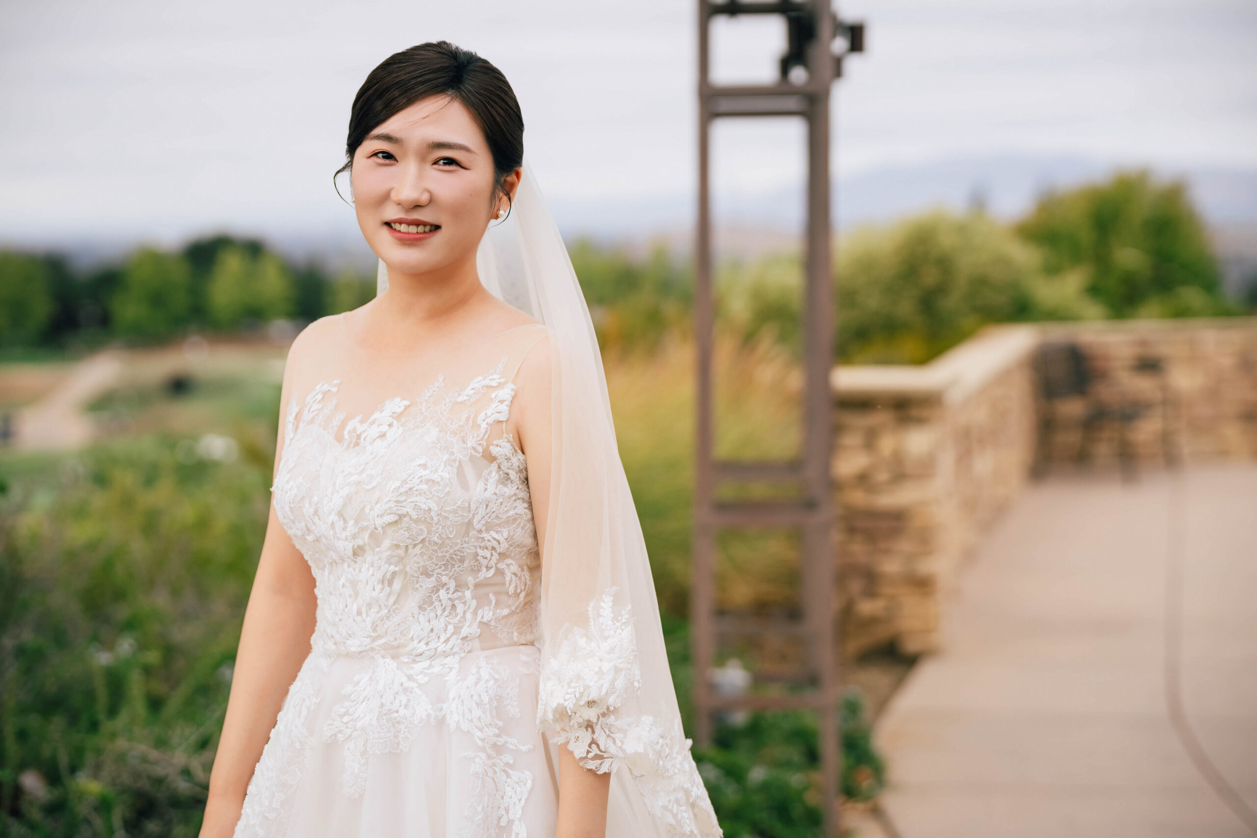 Bride smiling outdoors in a lace wedding gown and veil.