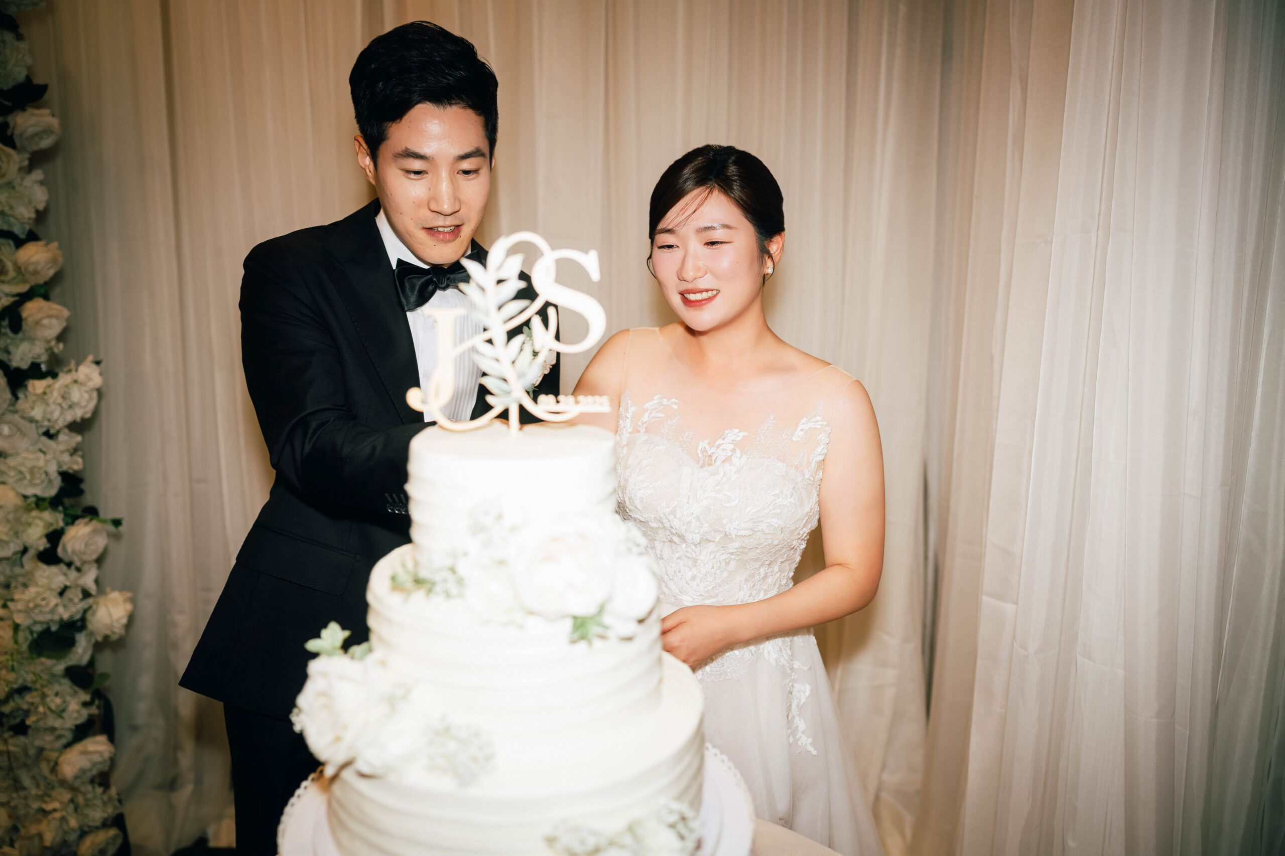Newlyweds cutting their white tiered wedding cake together.