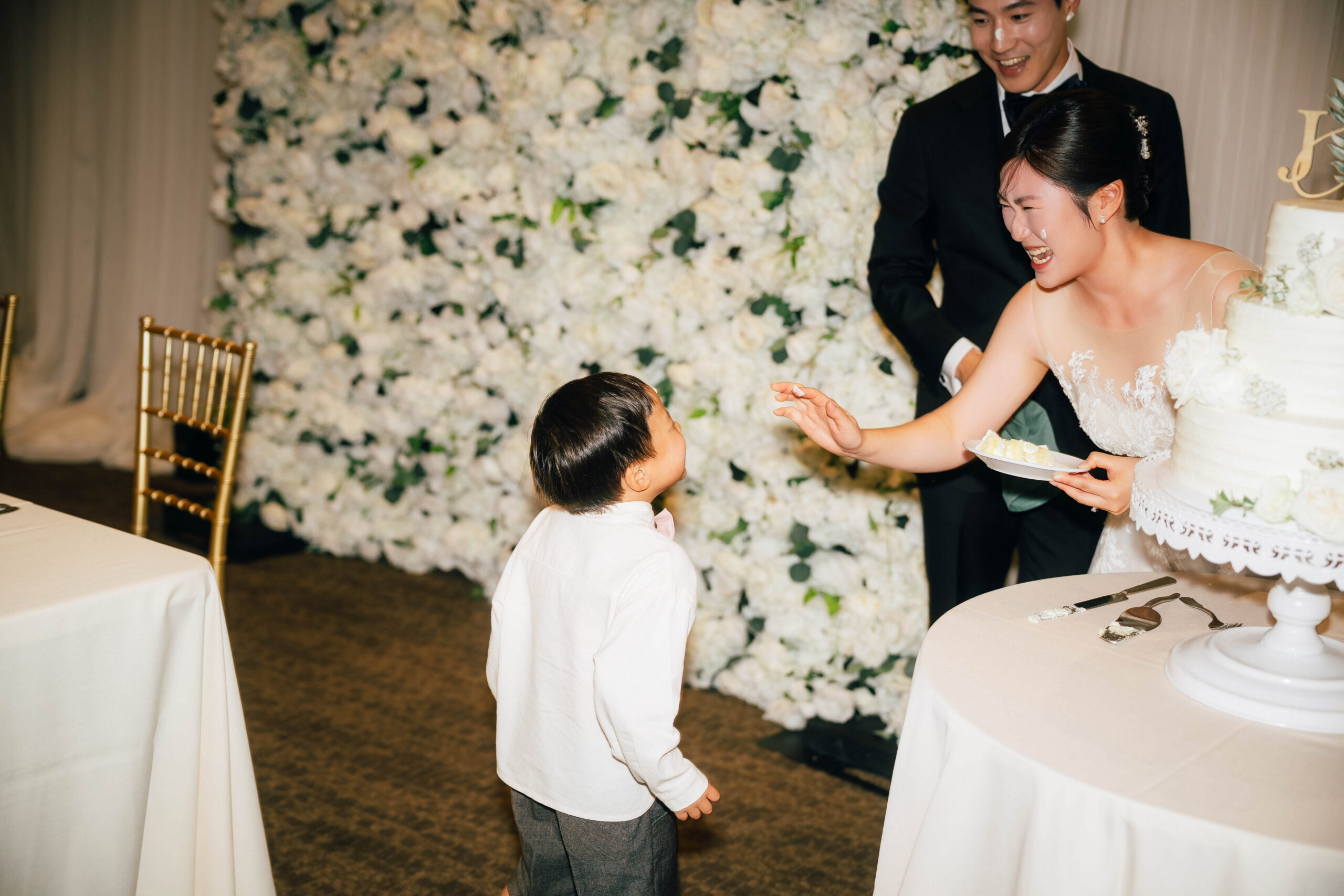 Bride laughing with a young guest beside the wedding cake.