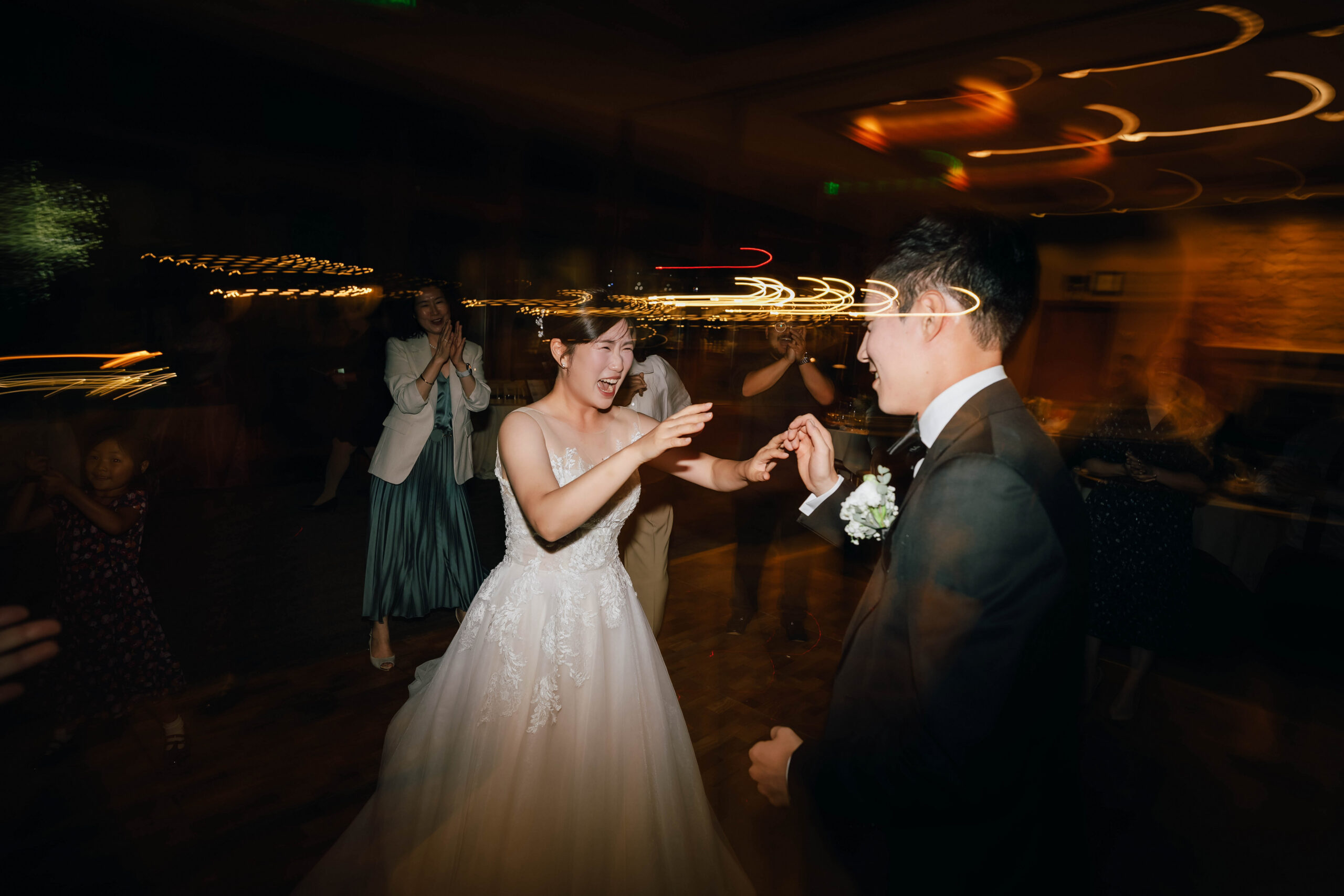 Bride laughing as she dances with the groom beneath warm light trails.