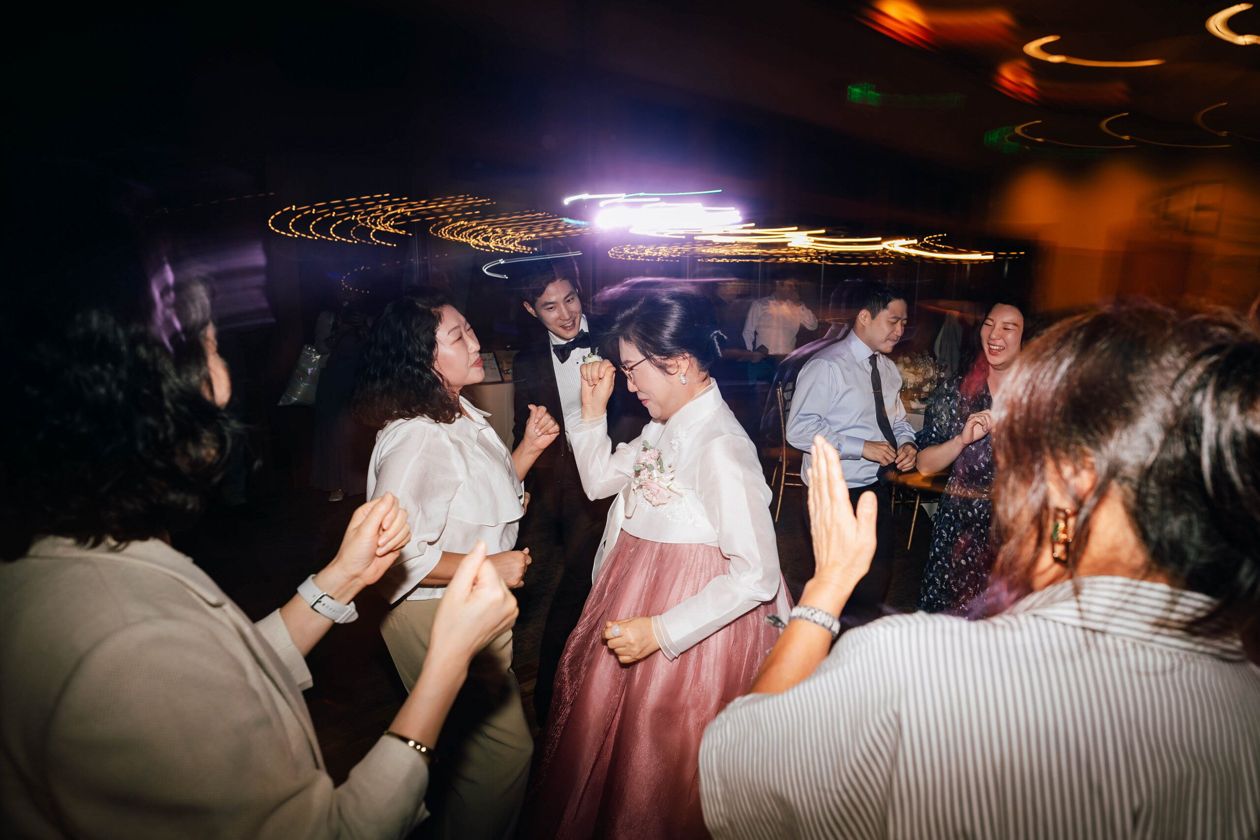 A woman in a pink and white hanbok dancing with guests around her.