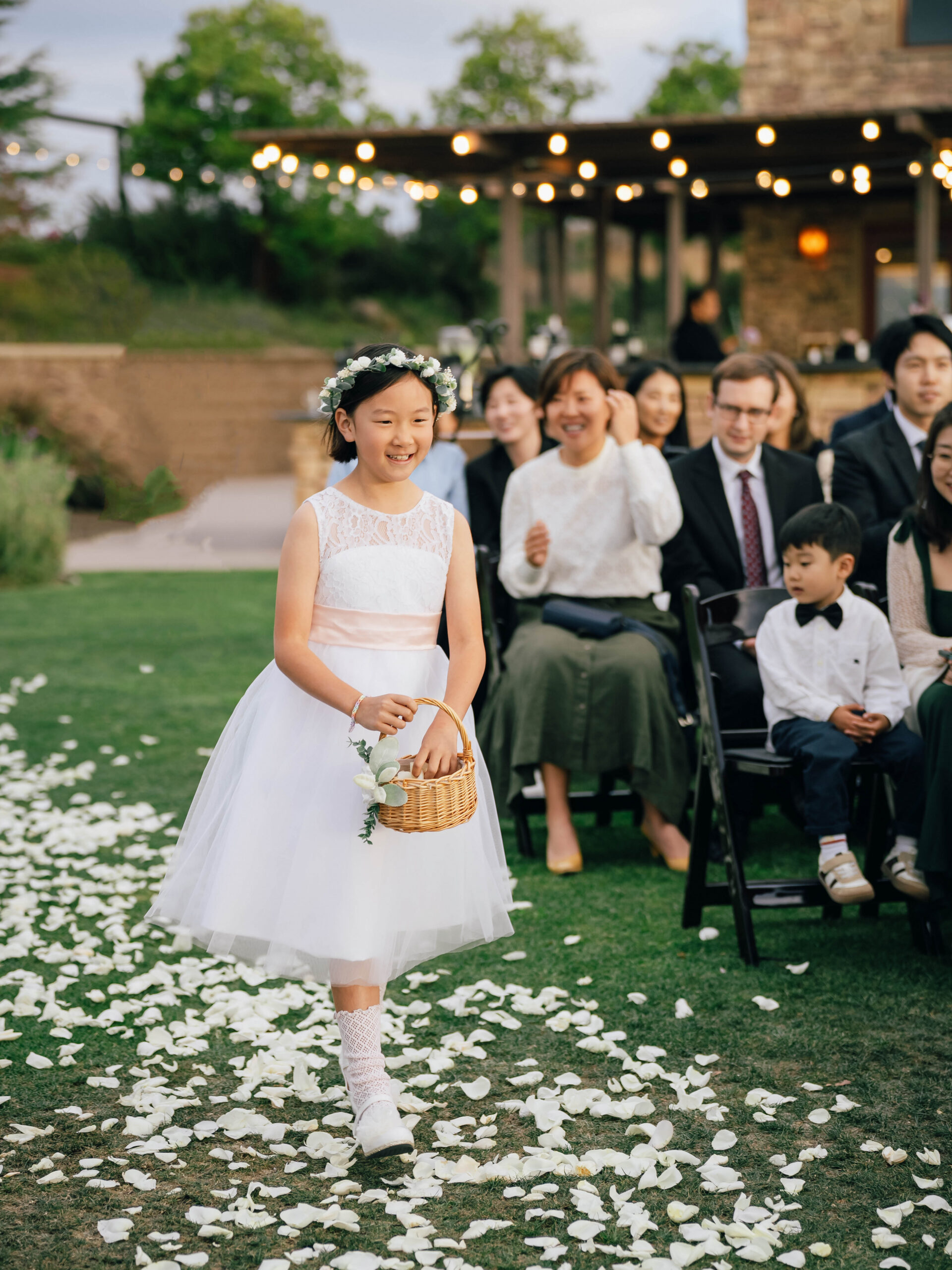 Flower girl carrying a wicker basket down the petal-covered aisle.