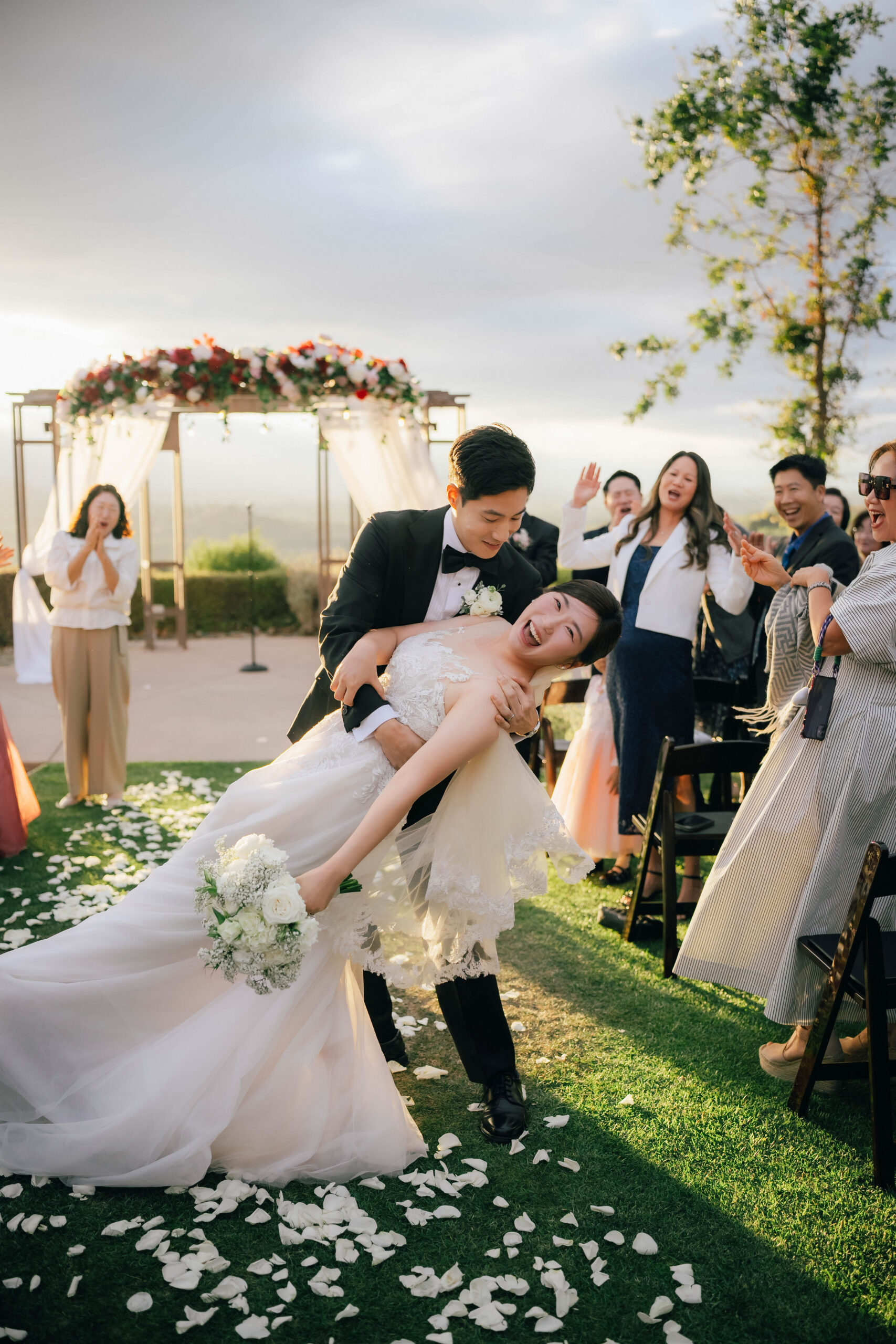 Groom dipping the laughing bride in the aisle as their guests cheer.