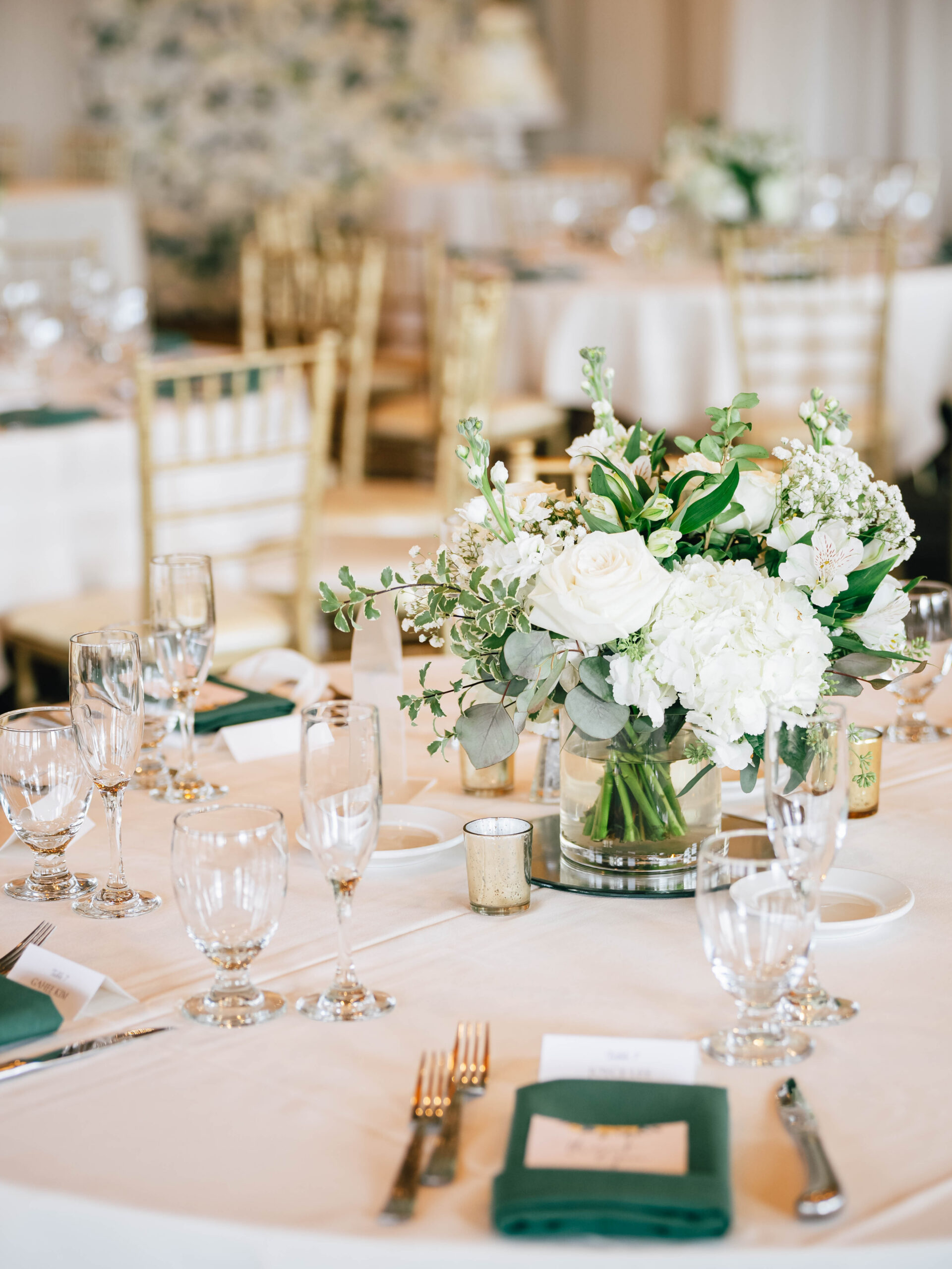Reception table with white flowers, green napkins and glassware.
