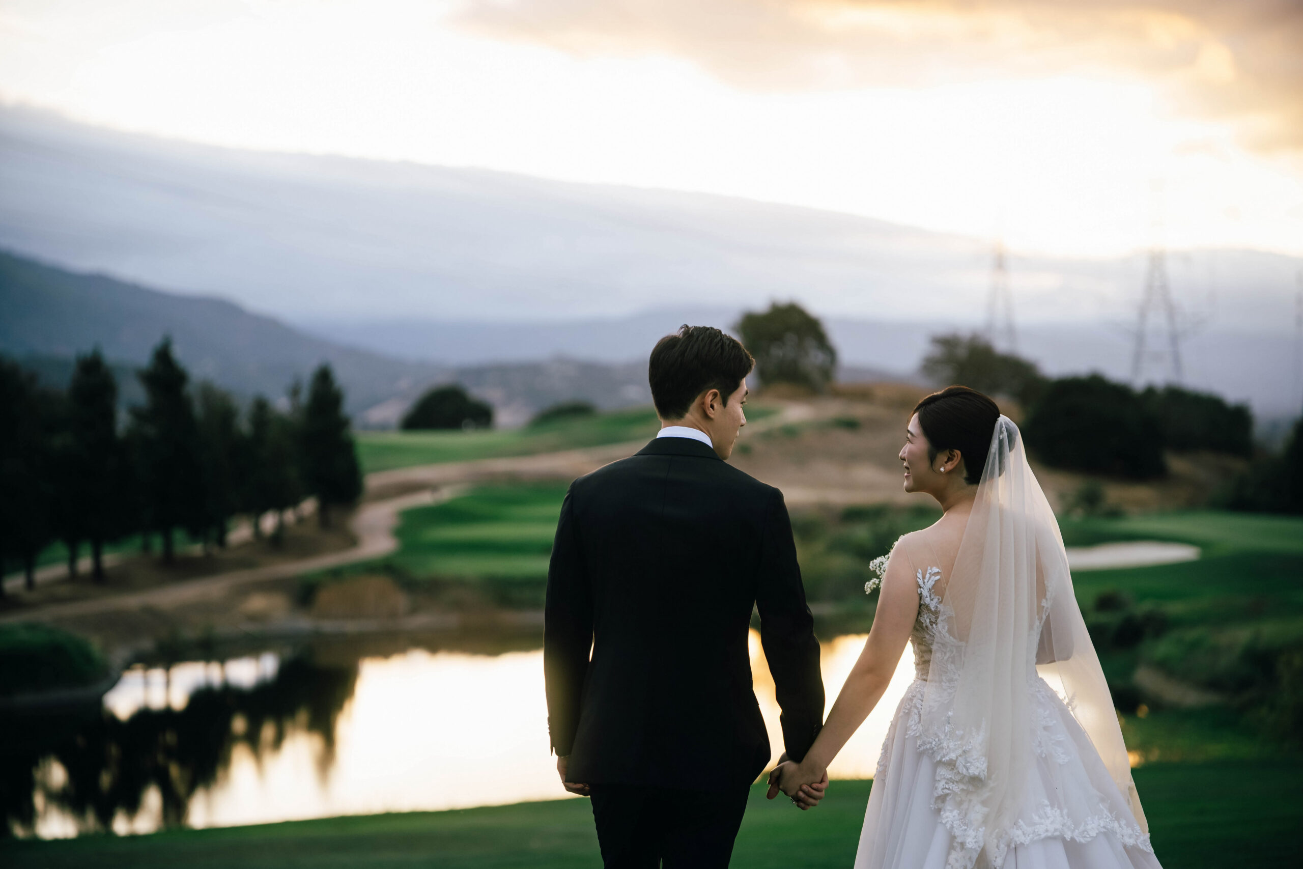 Newlyweds holding hands beside the golf course pond at sunset.