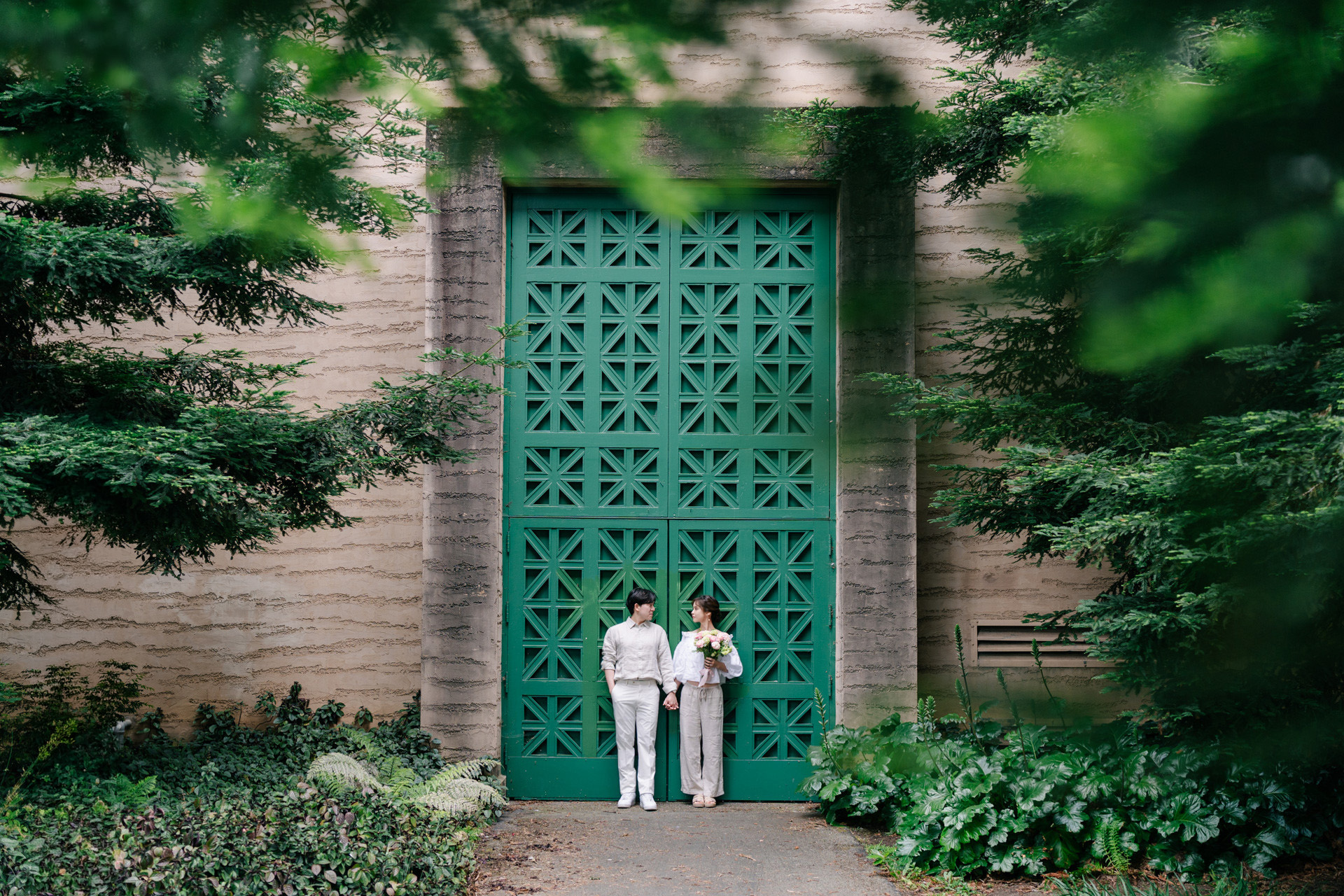 Couple holding hands beneath a tall green patterned door framed by foliage.
