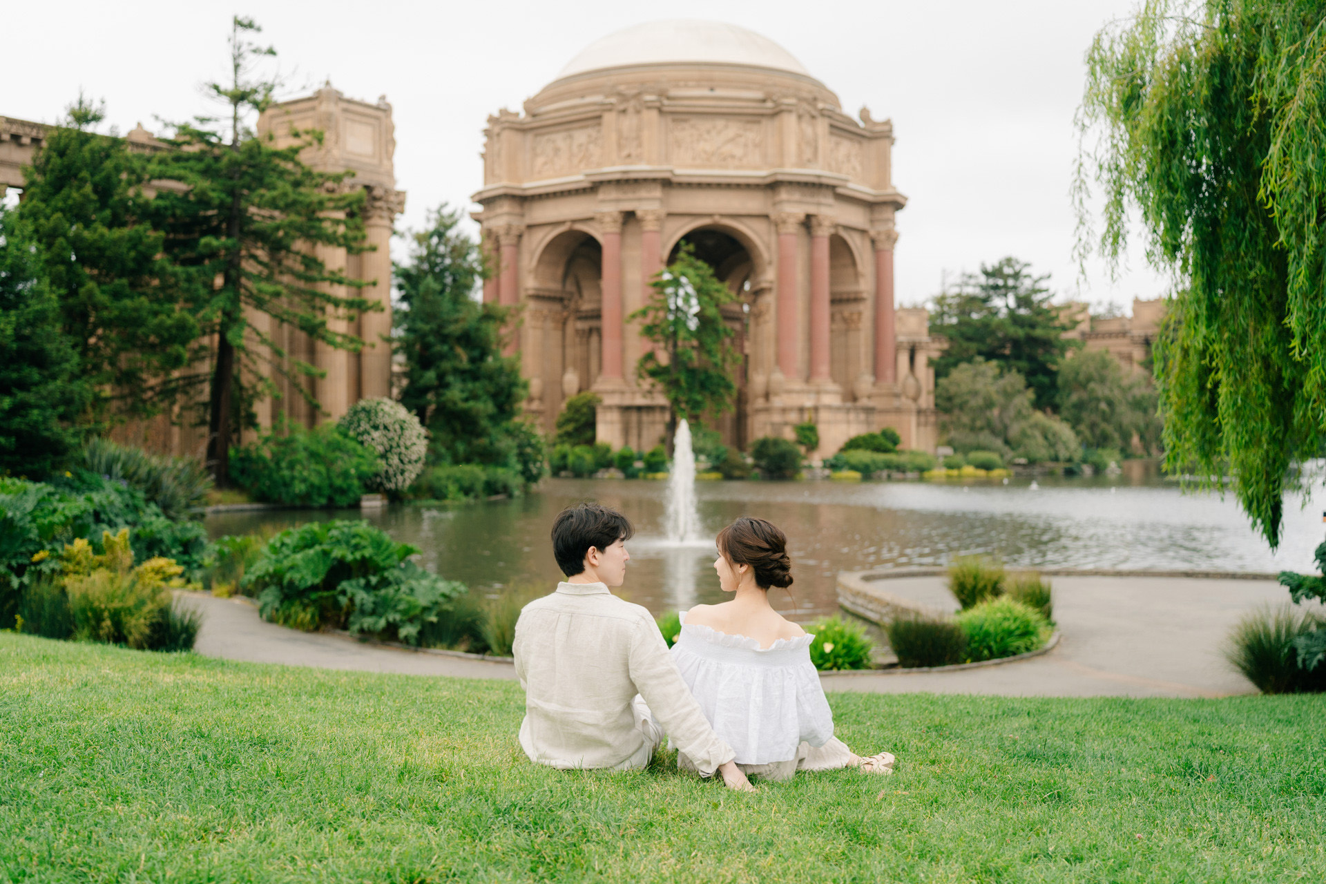 Couple sitting together on grass overlooking the lake and Palace of Fine Arts.