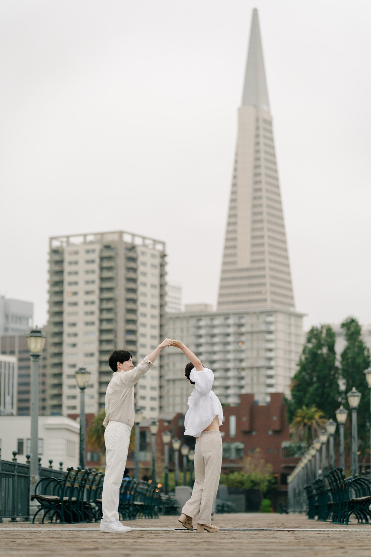 Couple twirling on a San Francisco pier with the Transamerica Pyramid behind them.