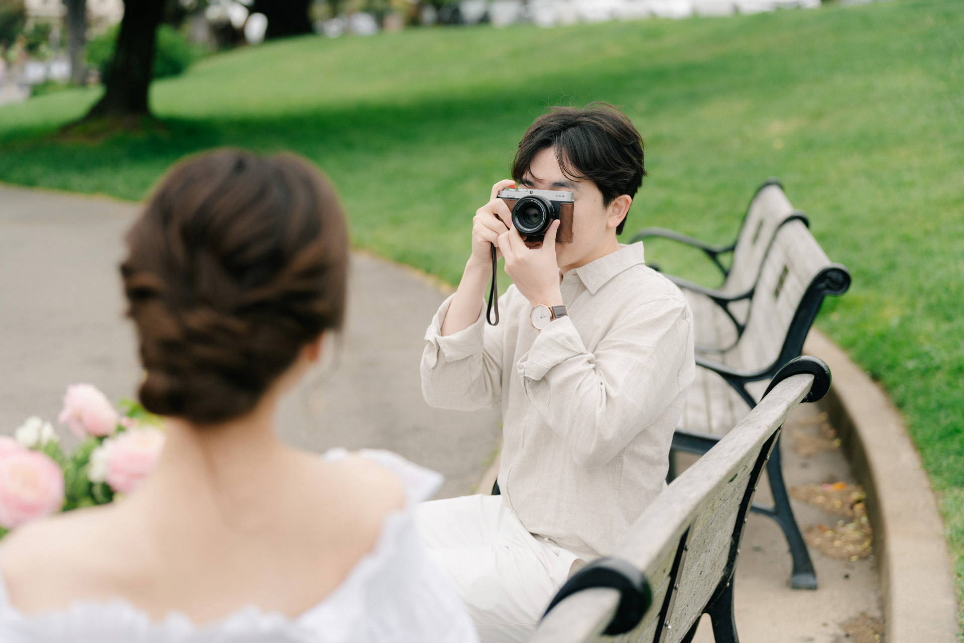 Man taking a photograph of his partner while seated on a park bench.