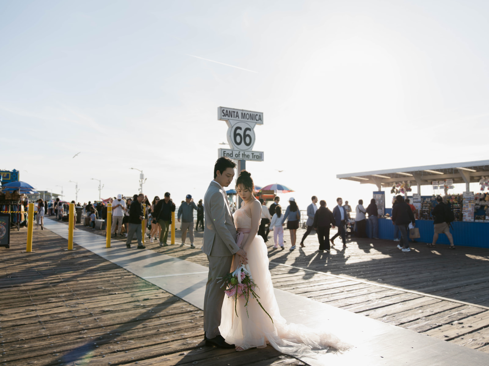 Couple holding hands beneath the Route 66 End of the Trail sign on Santa Monica Pier.