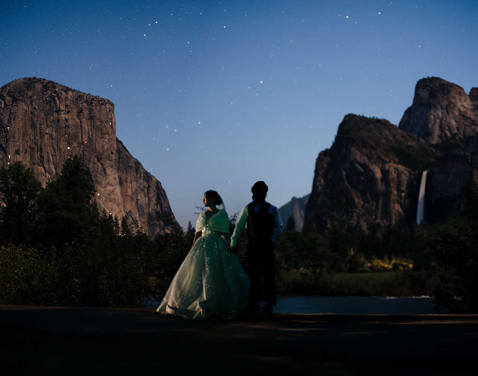 Wedding couple silhouetted beneath stars between granite cliffs, with a waterfall in the distance.