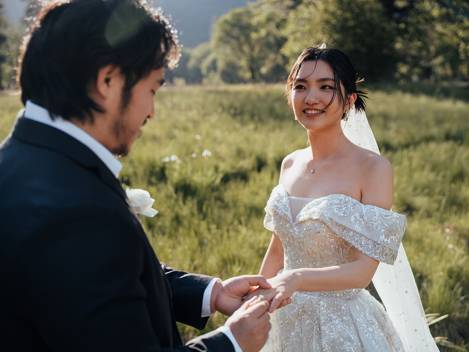 Close view of a wedding ring exchange in a sunlit meadow.