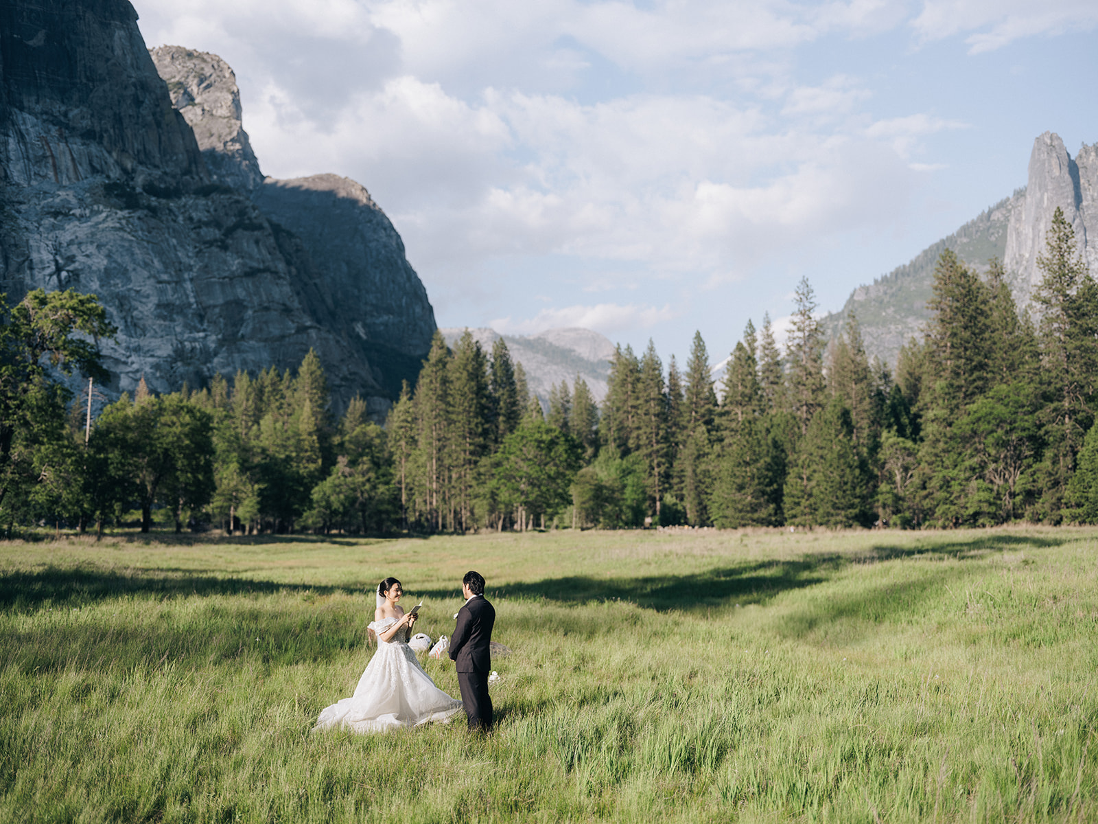 Wedding couple facing each other with vow books in a meadow beneath granite cliffs.
