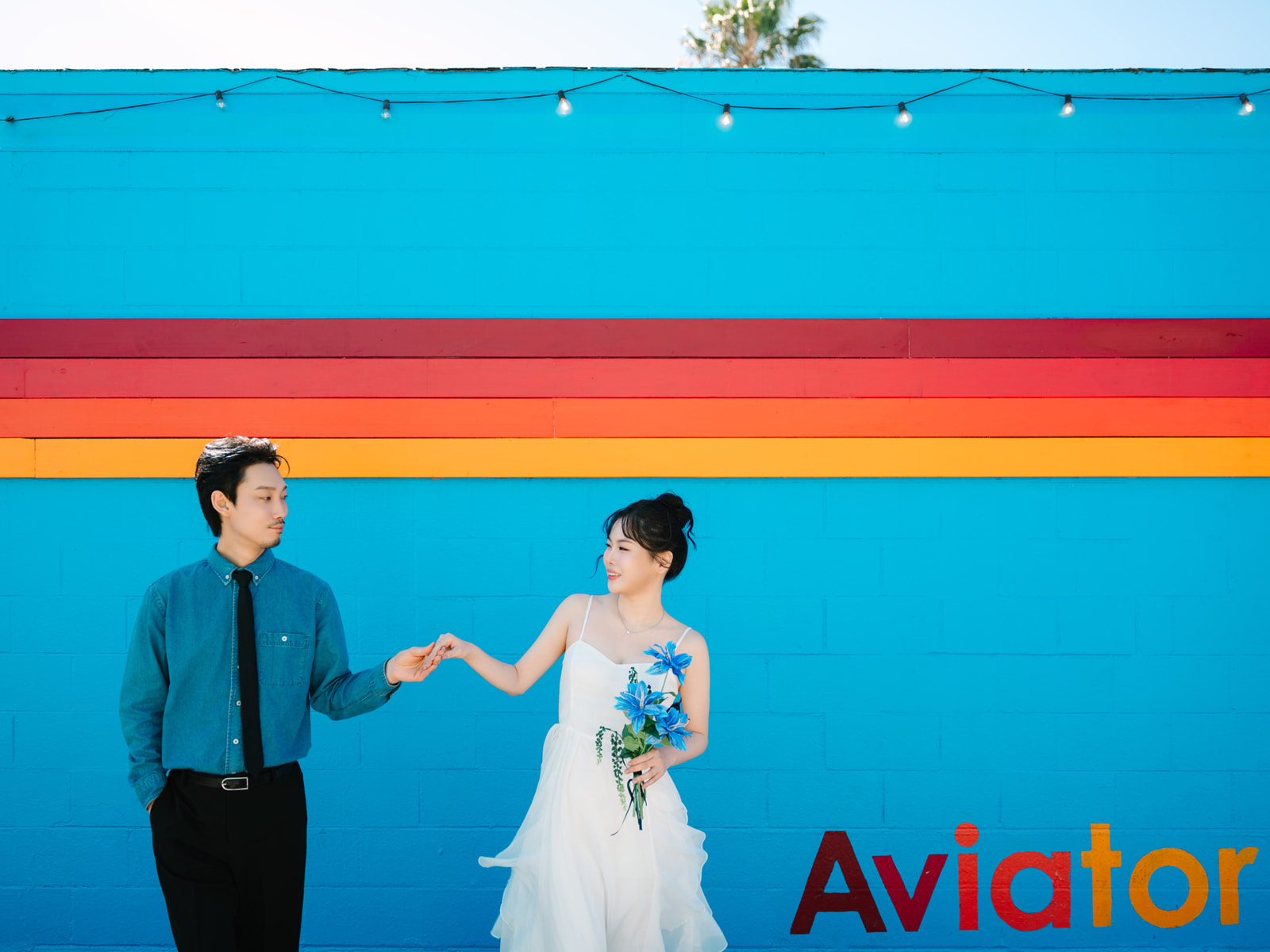 Couple joining hands in front of a turquoise wall with colorful stripes
