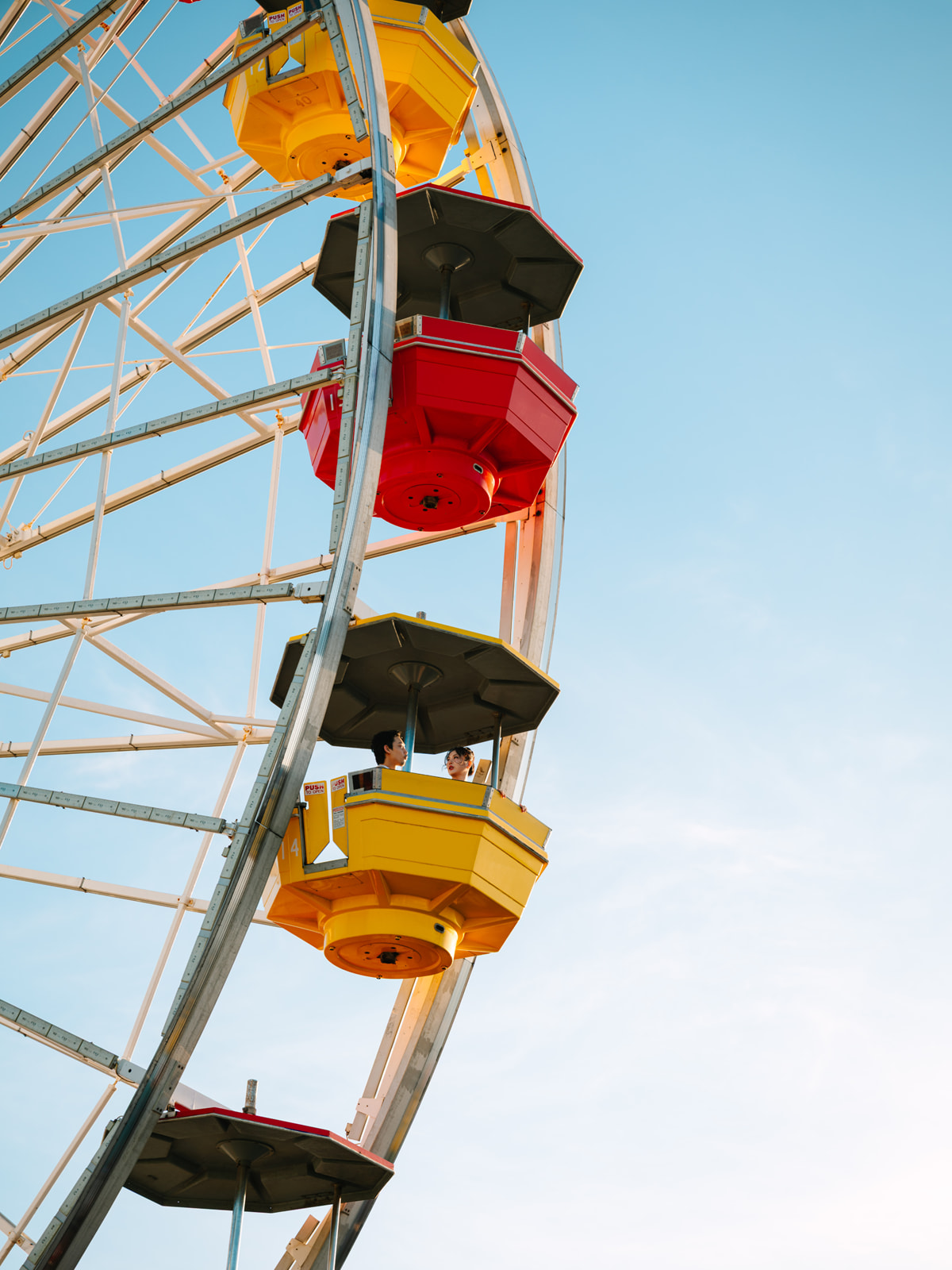 Couple riding in a yellow Ferris wheel gondola against a blue sky