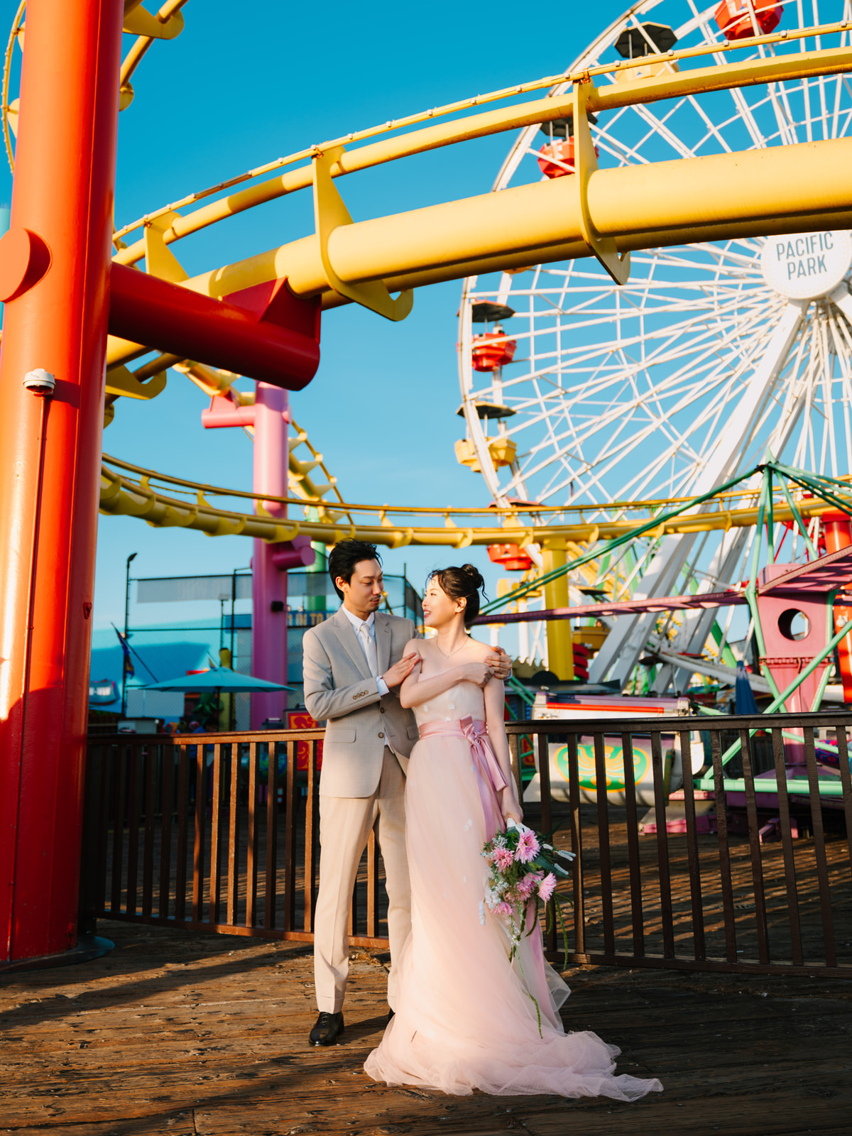 Couple embracing beneath colorful roller coaster tracks and the Ferris wheel