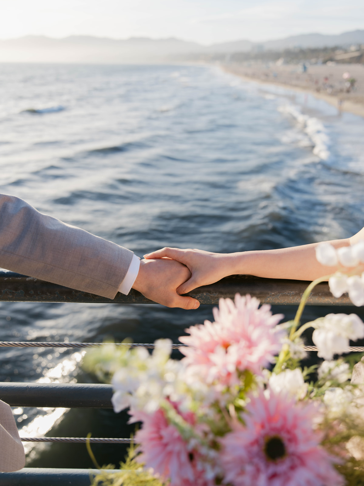Close-up of a couple holding hands at the pier railing above the ocean
