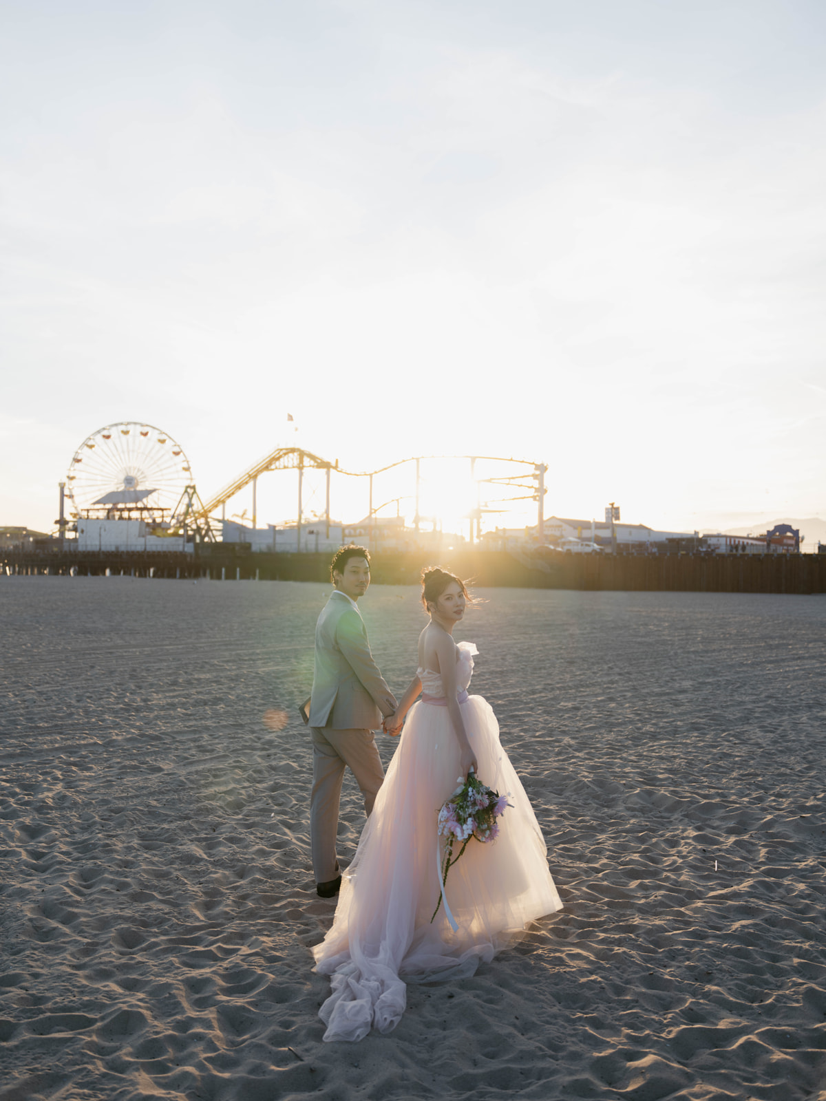 Couple looking back while holding hands on the beach at sunset