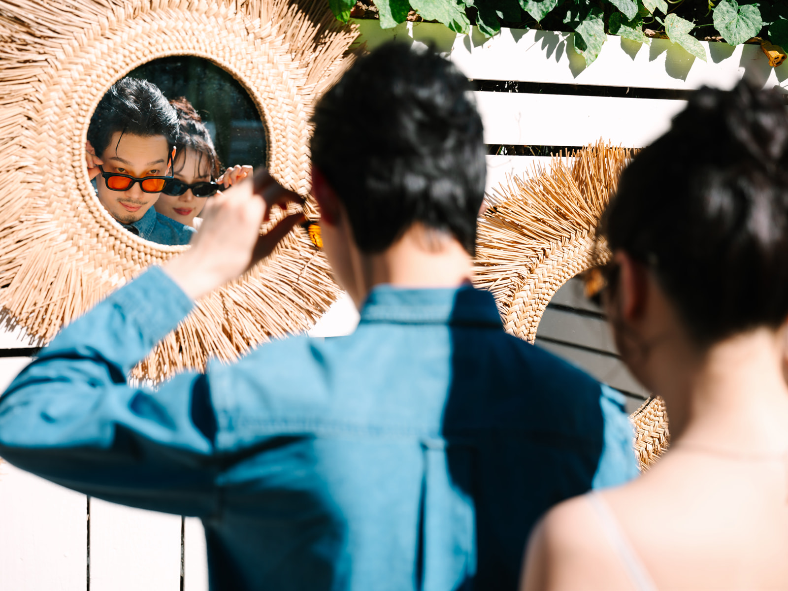 Couple lowering their sunglasses in a round woven mirror